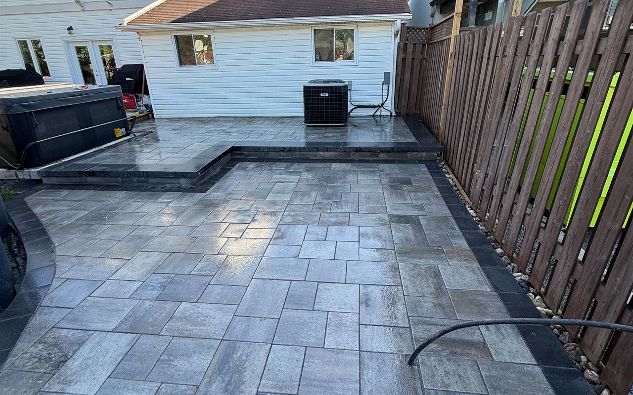 Finished multi-level interlock patio with charcoal borders and clean shed siding