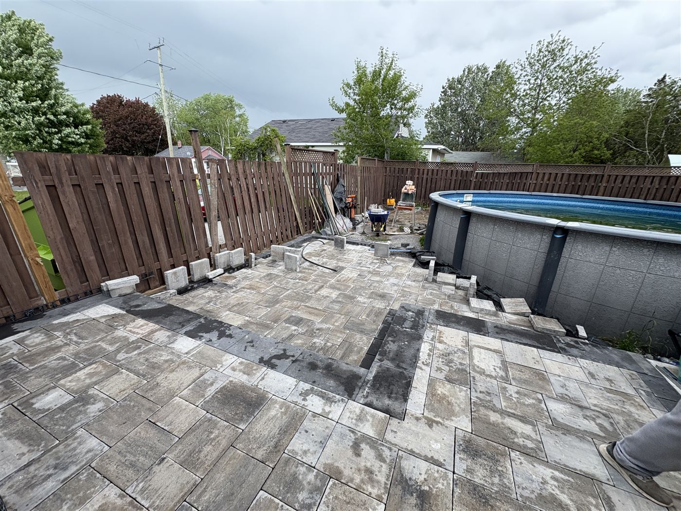 Grey interlock patio built around an above-ground pool with a charcoal border